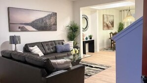 A modern living room with a dark leather sofa, a glass coffee table, and a large landscape painting on the wall. - Modern Retreat 3BR 2&half Bath (Edmonton)