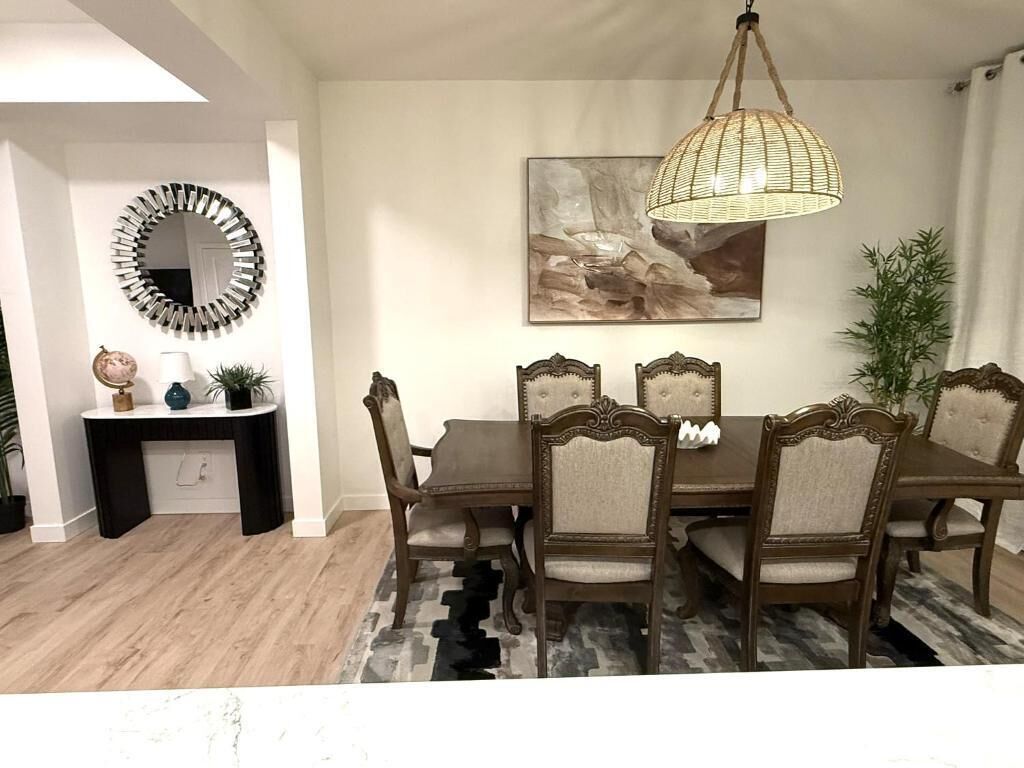 A dining room with a round table, six chairs, a hanging light fixture, a mirror, and a painting on the wall.