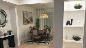 A modern dining area with a wooden table and chairs, a pendant light, and a white wall with shelves. - Modern Retreat 3BR 2&half Bath (Edmonton)