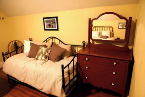 Una cama con cabecera, un aparador con cajones, una silla y un cuadro enmarcado en la pared.