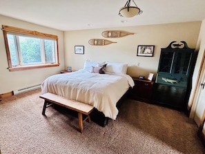 Une chambre à coucher comprenant un lit, un banc, des tables de chevet, une commode, une fenêtre et des éléments de décoration murale.