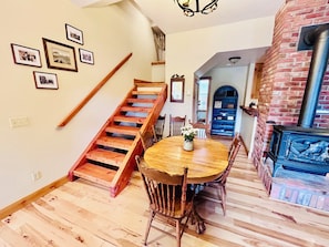 A wooden staircase, a dining table with chairs, a brick fireplace, and framed pictures on the wall.