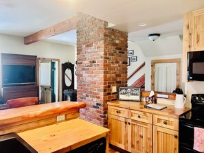 Une cuisine avec des meubles en bois, une colonne en briques, une table à manger en bois, un four à micro-ondes et une cuisinière.