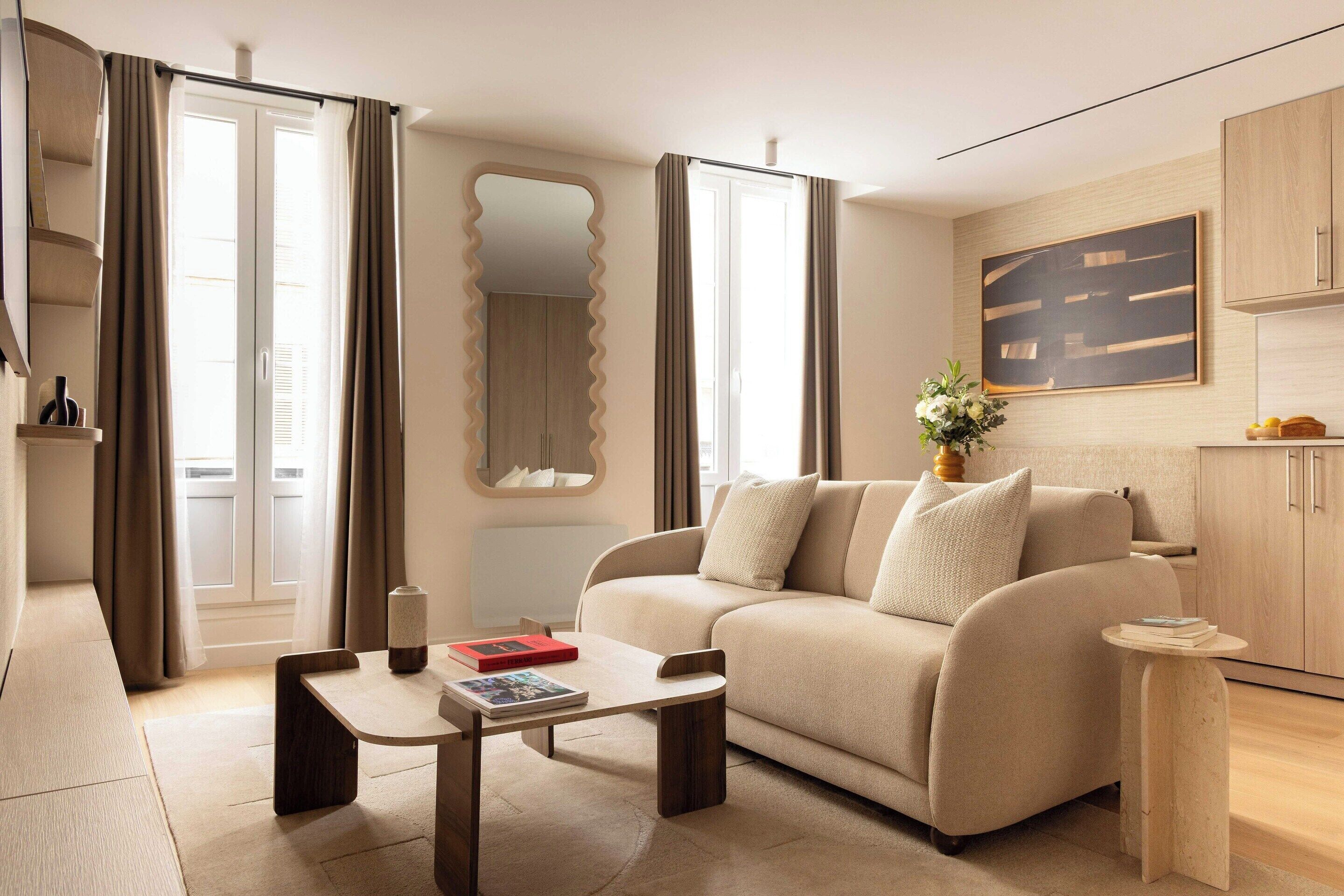 A modern living room with a sofa, a coffee table, a small side table, a mirror, and a painting on the wall.