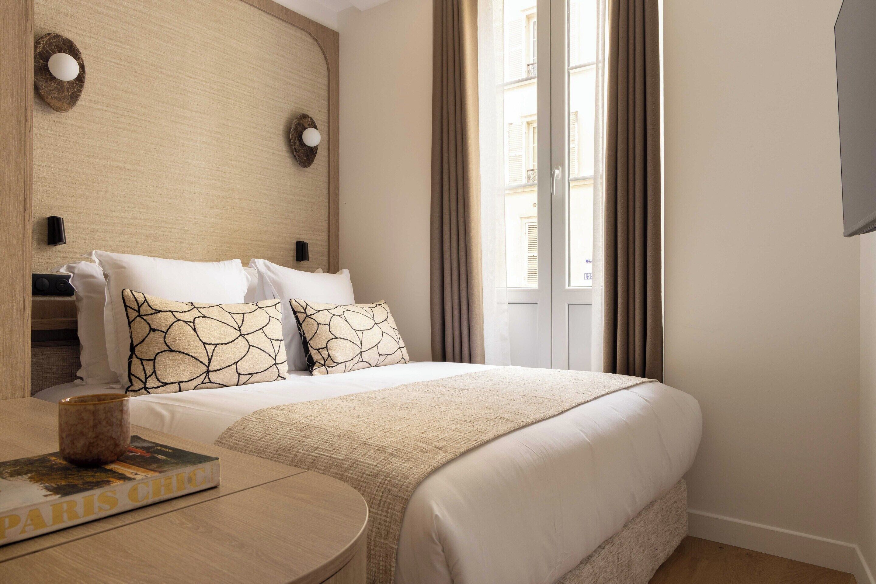 A hotel room with a large bed, a round wooden table, and a book titled 'PARIS CHIC'.