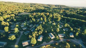 An aerial view of a campground with multiple cabins, surrounded by dense forest and hills.