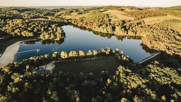 An aerial view of a lake surrounded by dense forest, with a road and a small building near the water.