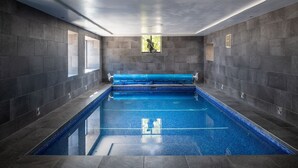Una piscina interior moderna con suelo de azulejos azules, paredes grises y un tragaluz.