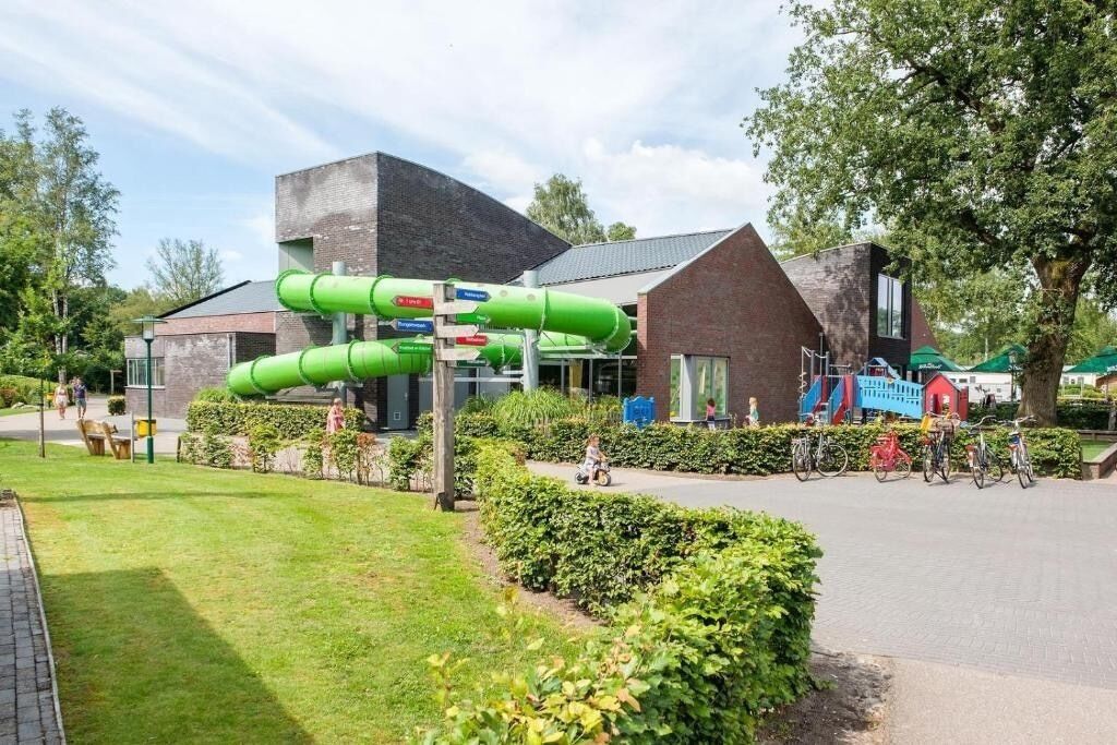 Een modern gebouw met een groene glijbaan, een bakstenen structuur en een geplaveid gebied met fietsen.