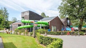 A modern building with a green water slide, a brick structure, and a paved area with bicycles. - De Ankergooi! (Hardenberg)