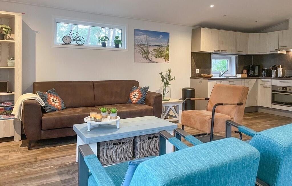 Een moderne woonkamer met een bruine bank, blauwe fauteuils, een salontafel en een keuken op de achtergrond.