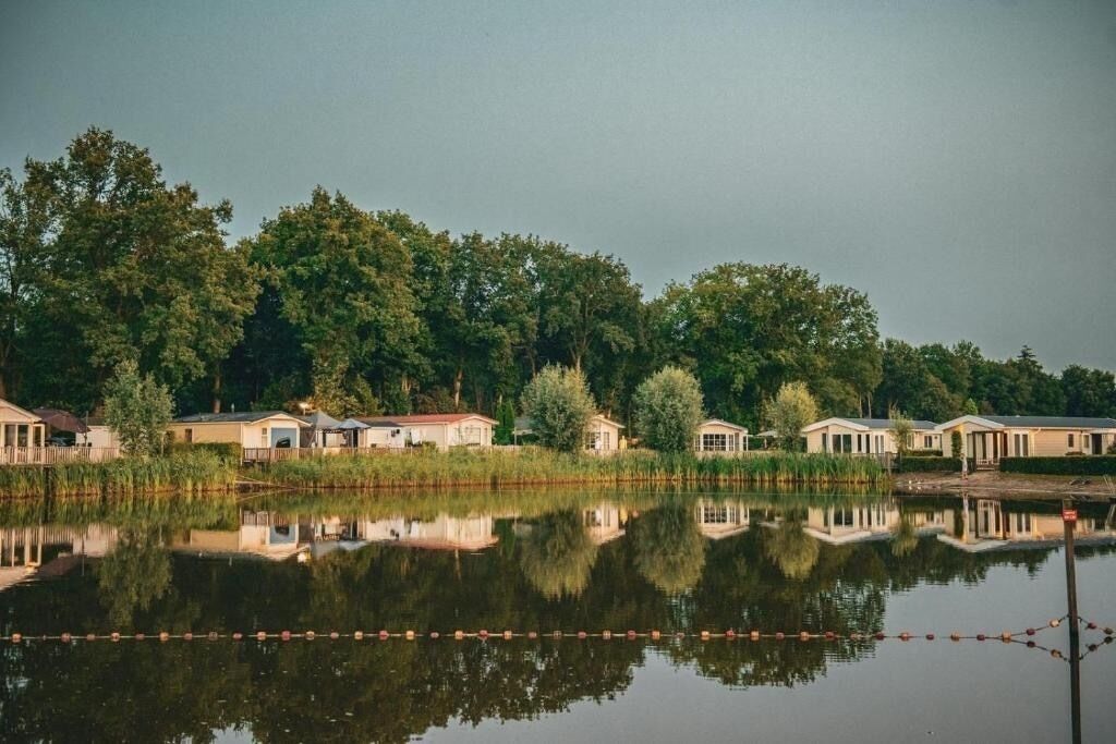 Een landgoed aan het meer met meerdere huisjes, een aanlegsteiger en de reflectie van de huisjes in het water.