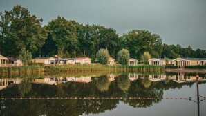 A lakeside property with multiple cabins, a dock, and a reflection of the cabins in the water. - De Ankergooi! (Hardenberg)