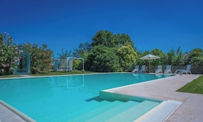 A clear swimming pool with a diving board, lounge chairs, and a small covered area.