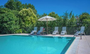 A swimming pool with lounge chairs and an umbrella, surrounded by greenery.