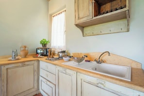 A kitchen with a sink, countertop, cabinets, and a window with curtains.