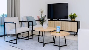 A modern living room with a sofa, two armchairs, a coffee table, a TV, a cabinet, and a potted plant. - Apartment in Breskens Near the Beach (Breskens)