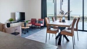A modern hotel room with a large window, a flat-screen TV, a dining area, and a seating arrangement. - Apartment in Breskens Near the Beach (Breskens)