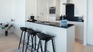 A modern kitchen with a central island, bar stools, a stainless steel range hood, and a potted plant. - Apartment in Breskens Near the Beach (Breskens)