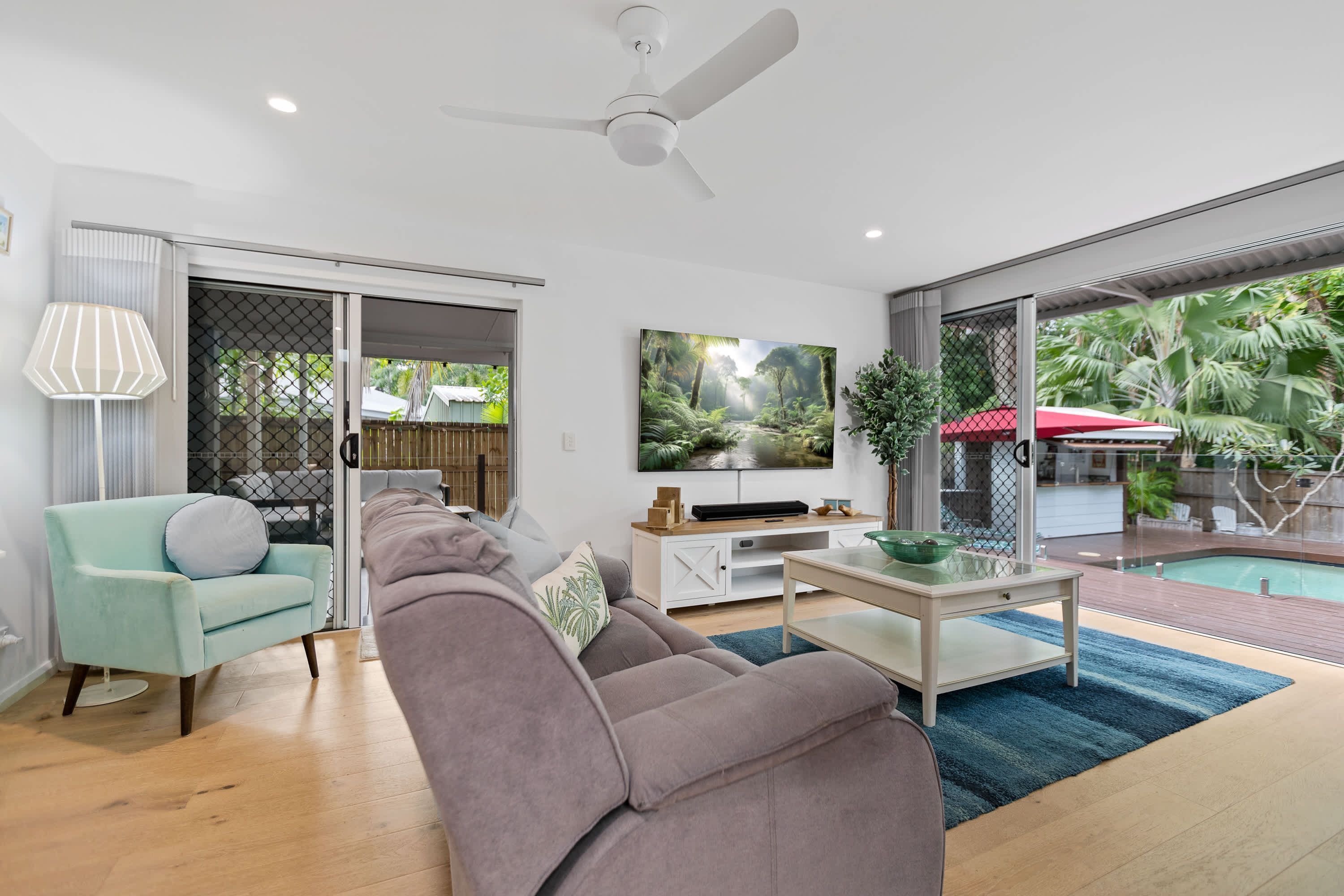 A modern living room with a sofa, TV, and a view of a pool.