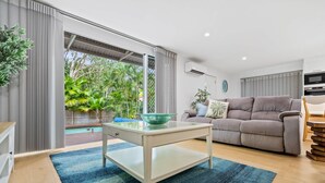 Sala moderna com mesa de centro de vidro, sofá cinza e vista para uma piscina e vegetação.