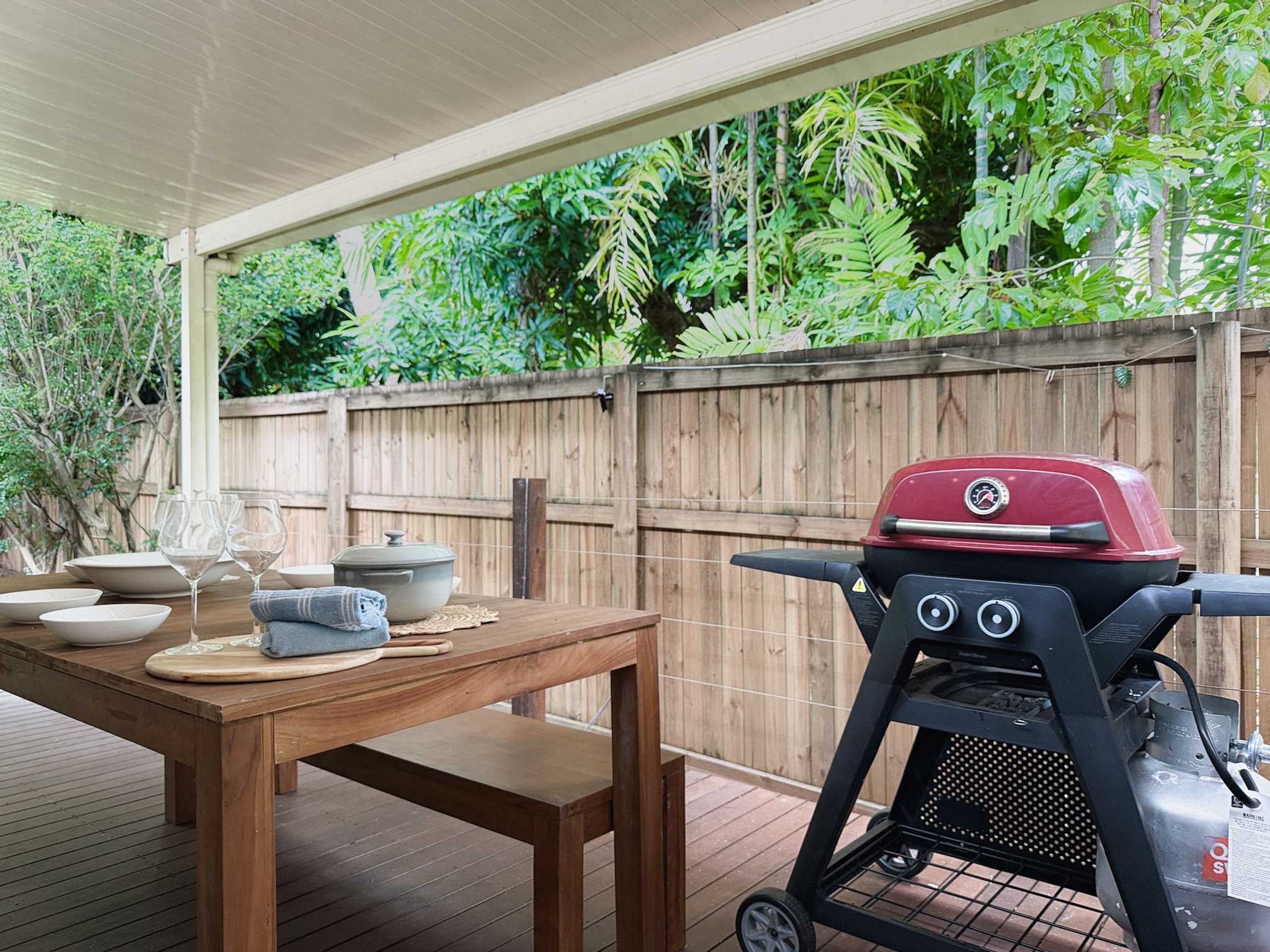 An outdoor patio with a wooden table, a barbecue grill, and a wooden fence.