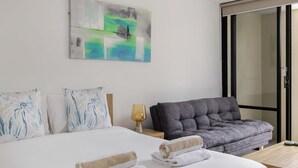 Quarto de hotel com cama, sofá cinza, mesa de madeira e um quadro na parede.