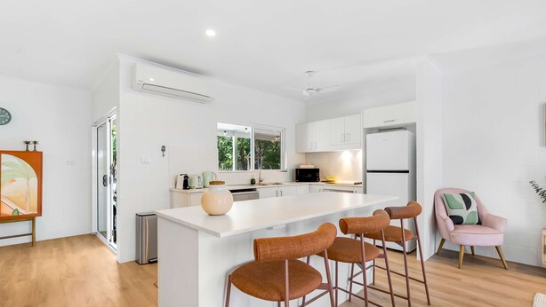 Een moderne keuken met witte kasten, een centraal eiland met krukken, en uitzicht op groen buiten.