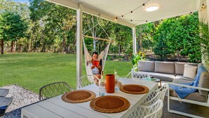 Een overdekt terras met een hangmat, een bank en een tafel met placemats en een vaas.