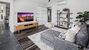 A modern living room with a large flat-screen TV, a grey sofa, a ceiling fan, and a wooden TV stand. - Rainforest Retreat Pool W Stunning Views (Cairns)