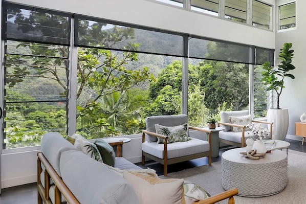 Una sala de estar moderna con ventanas amplias, un sofá, un sillón, una mesa de centro redonda y una planta en maceta.