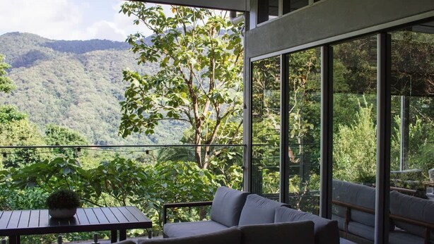 A balcony with a sofa and table, overlooking a lush green landscape with mountains. - Rainforest Retreat Pool W Stunning Views (Cairns)