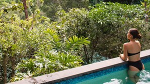 A person in a black swimsuit sitting on the edge of a pool surrounded by lush greenery. - Rainforest Retreat Pool W Stunning Views (Cairns)