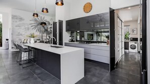 A modern kitchen with a central island, pendant lighting, and a large clock on the wall. - Rainforest Retreat Pool W Stunning Views (Cairns)