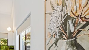 Een kamer met een houten bijzettafeltje, een schilderij van bloemen en uitzicht op groen.