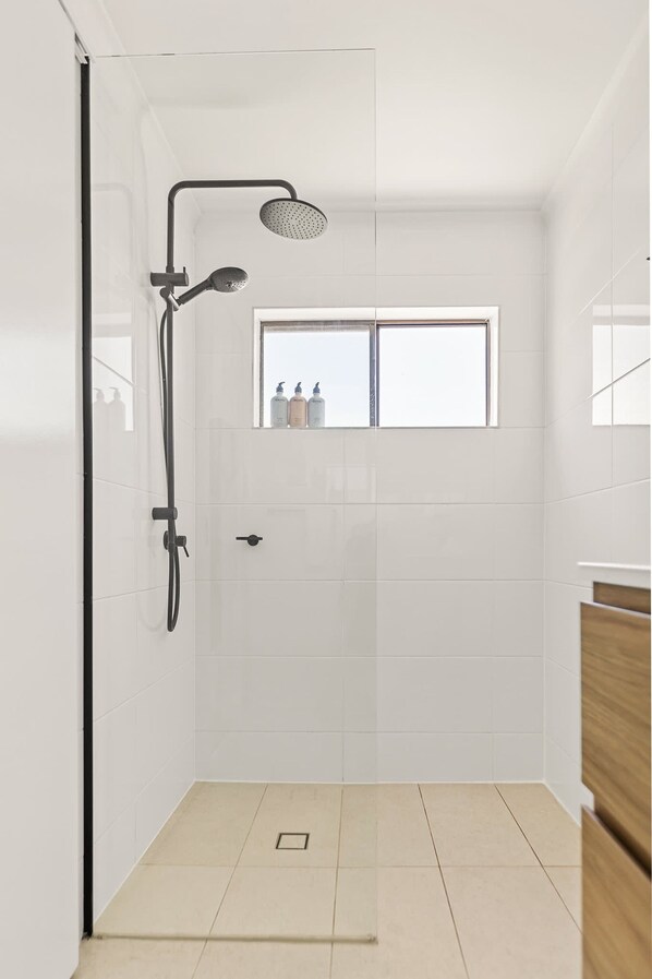 A modern shower with a handheld showerhead, a rain showerhead, and a window above the shower. - Spacious Whitfield Townhouse w Private Garden BBQ (Cairns)