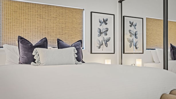 Een moderne hotelkamer met een groot bed, kunstwerken in lijsten aan de wanden, en een raam met een geweven vouwgordijn.