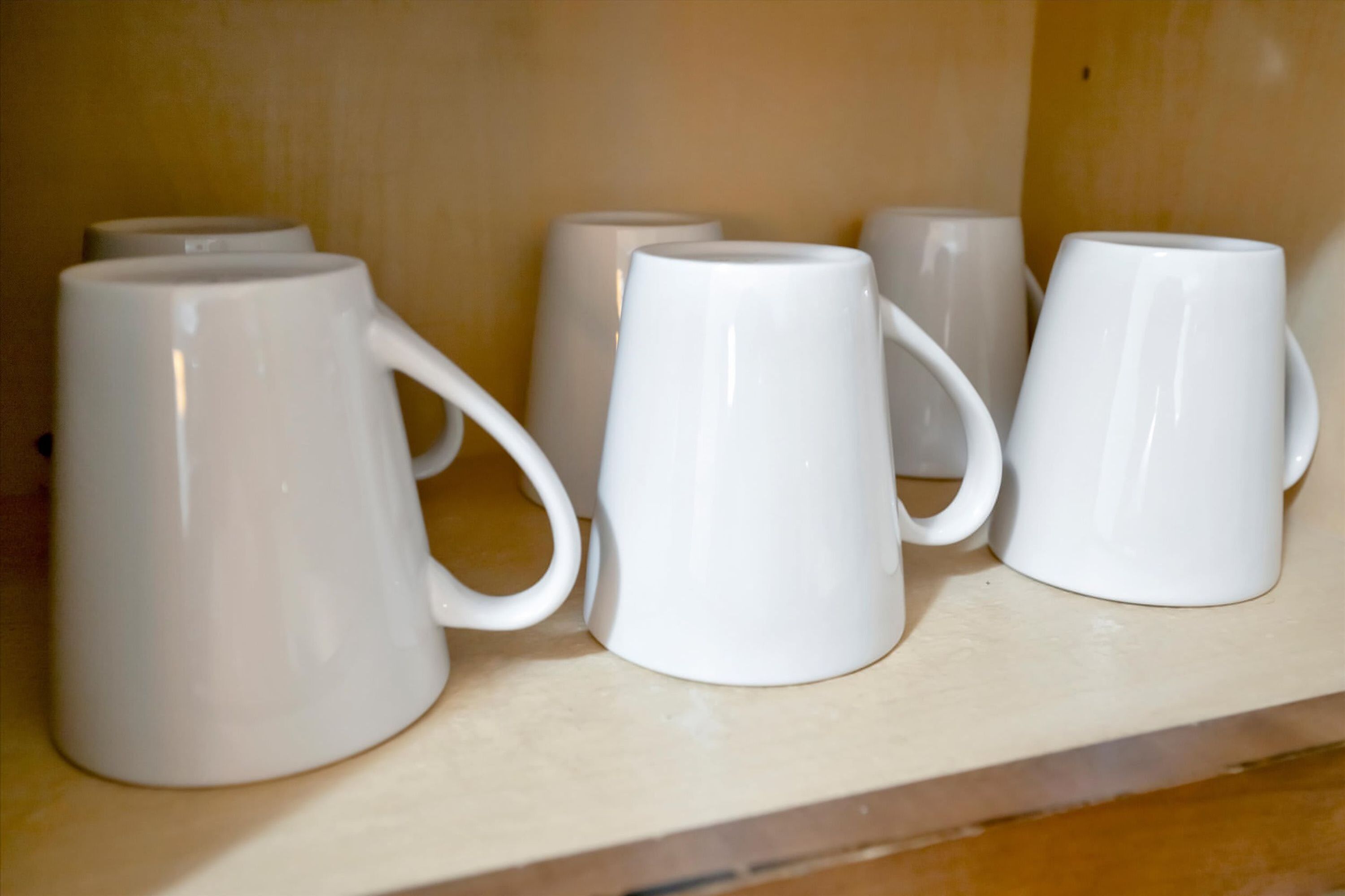 White ceramic mugs with handles on a shelf.