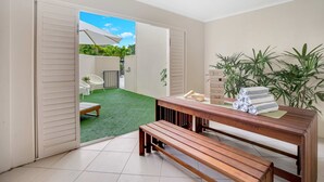 Ein Zimmer mit einer hölzernen Bank, einem Tisch mit Handtüchern und Blick auf eine grüne Rasenfläche und Terrassenmöbel.