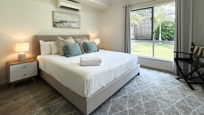 A bedroom with a bed, nightstands, an air conditioning unit, a ceiling fan, a window with a view, and a chair. - The Nook - Pet Family-friendly 4-bedroom (Cairns)