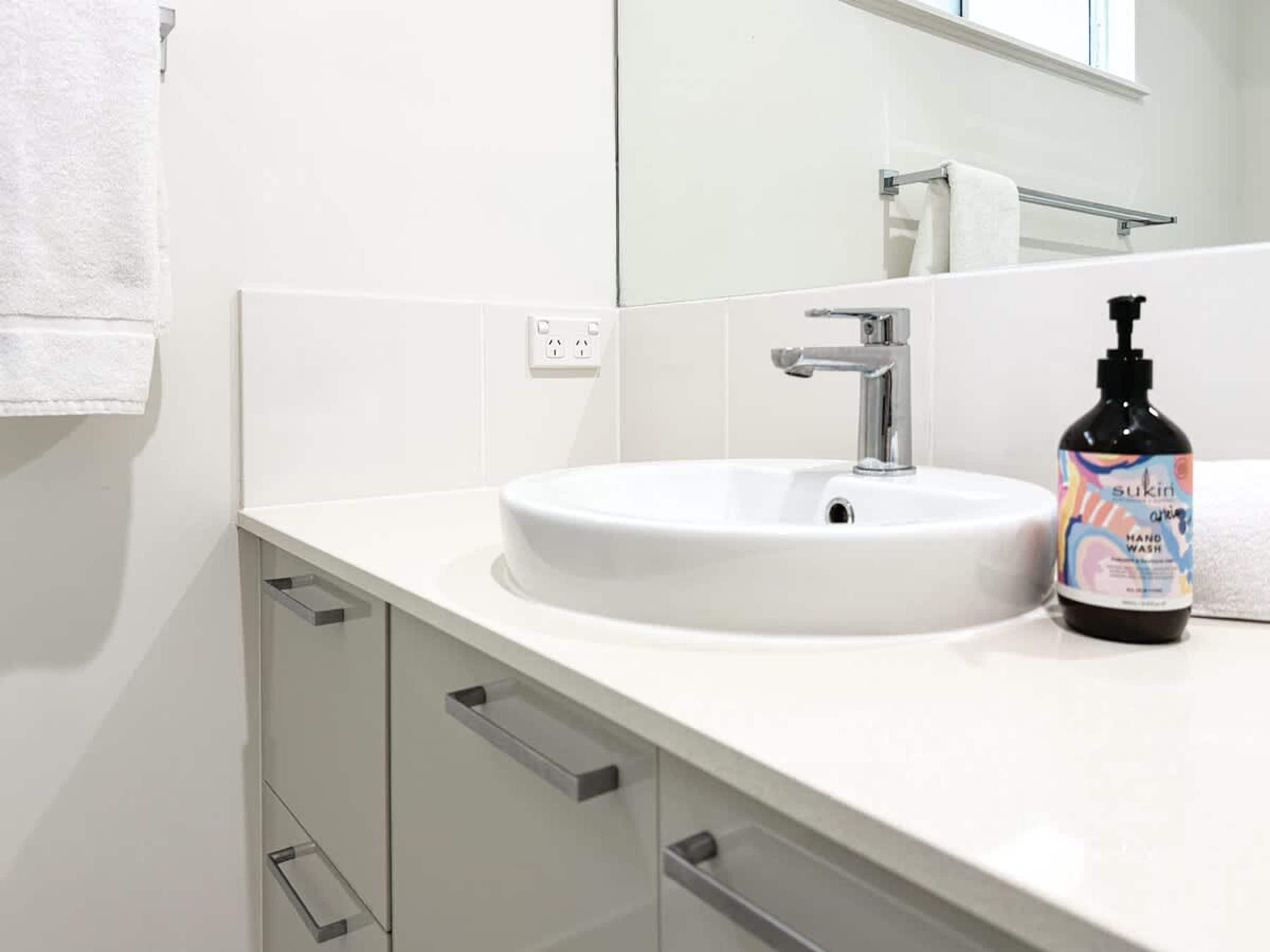 A bathroom with a white sink, a mirror, a towel, and a bottle of hand wash soap.