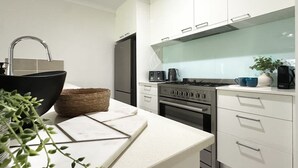 A modern kitchen with white cabinets, a black sink, a stainless steel refrigerator, and a gas stove. - The Nook - Pet Family-friendly 4-bedroom (Cairns)