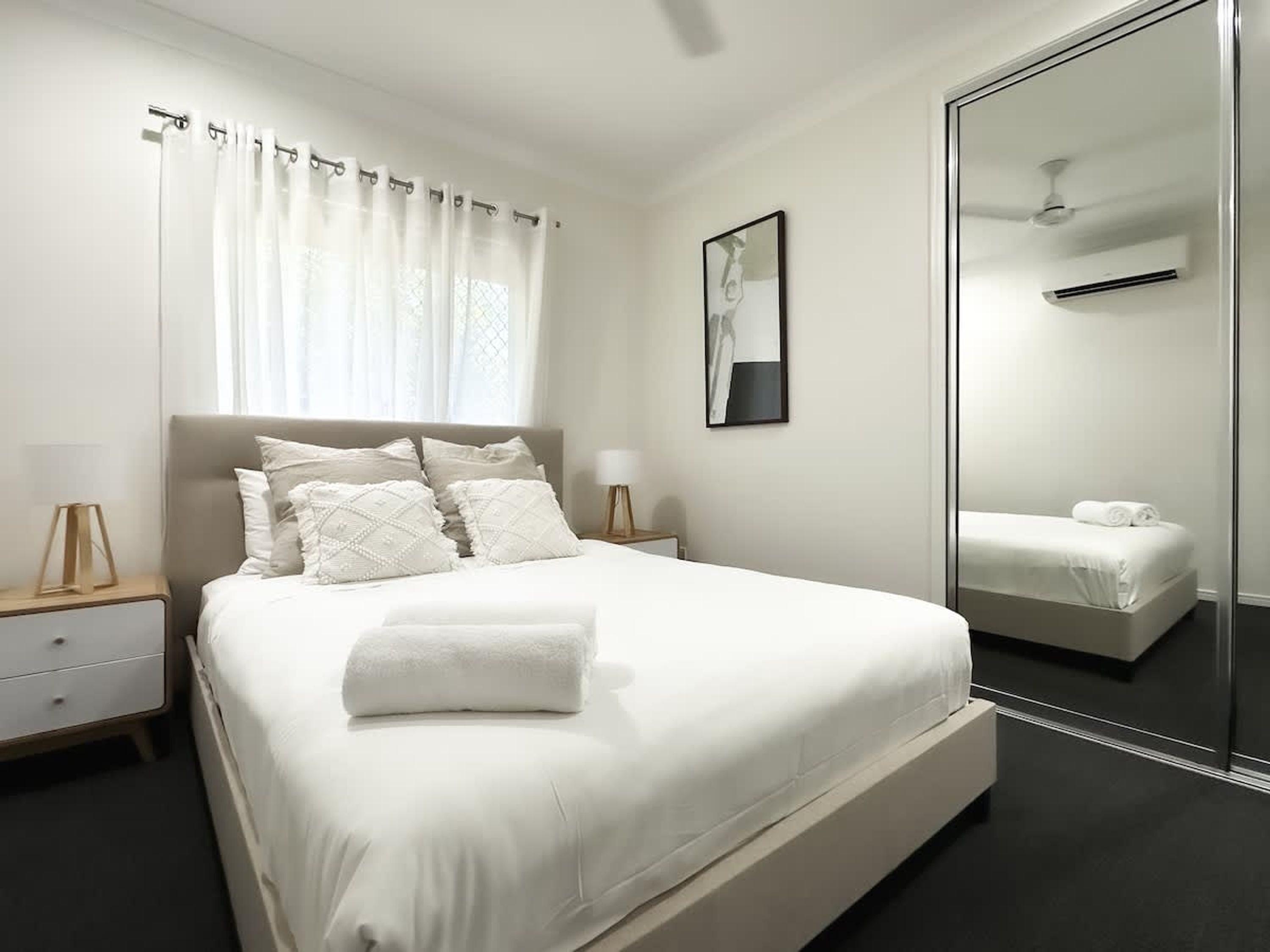 Un dormitorio moderno con una cama grande, una mesita de noche, un espejo y una ventana con cortinas.