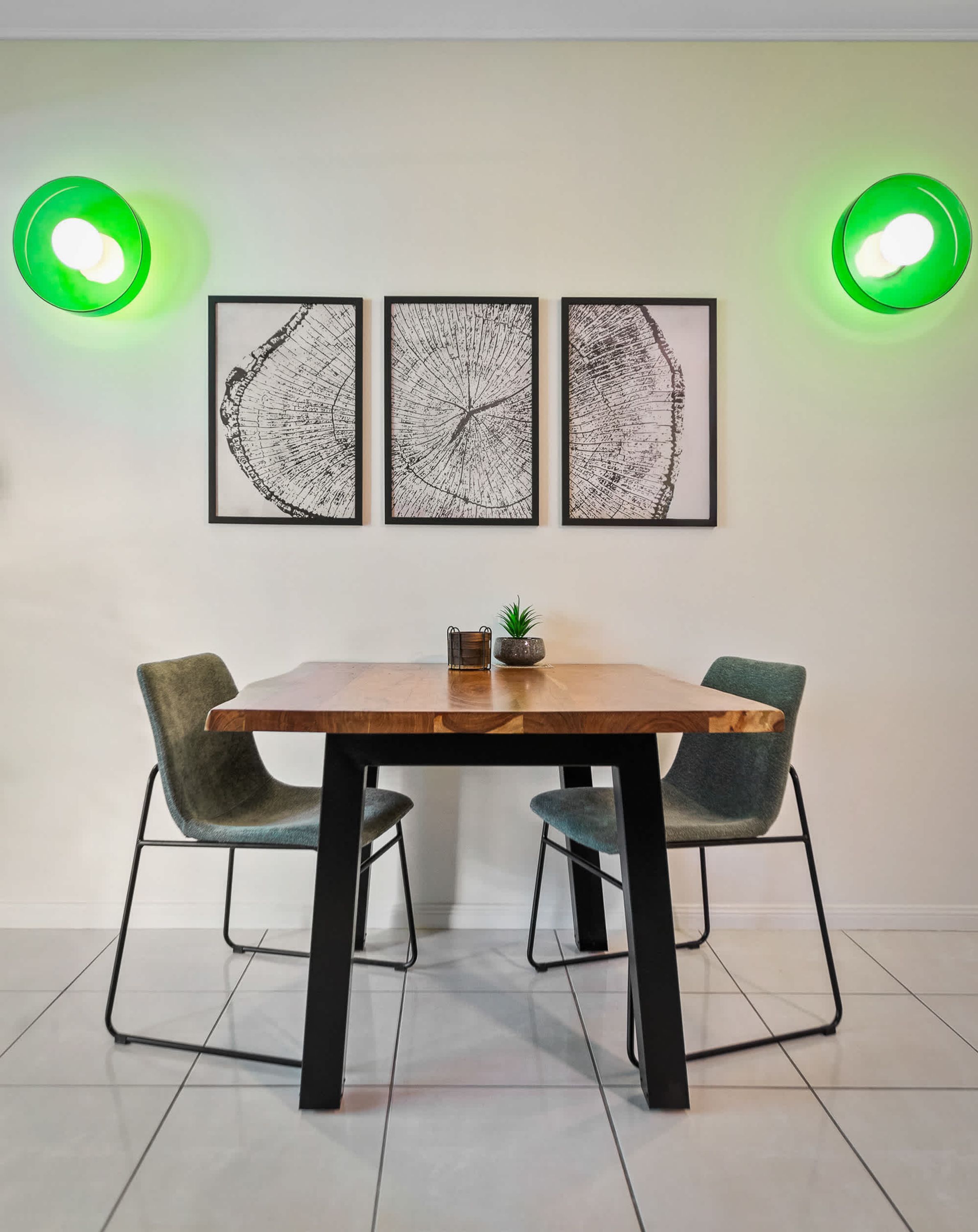 A dining area with a wooden table, two chairs, and three framed artworks on the wall.