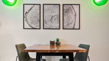 A dining area with a wooden table, two chairs, and three framed artworks on the wall.
