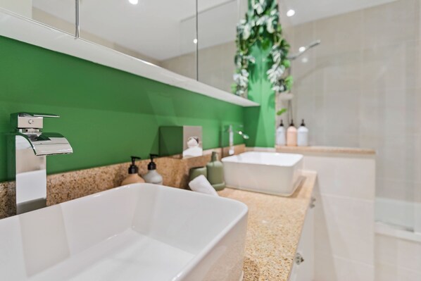 A modern bathroom with two sinks, a green accent wall, and a shower area.