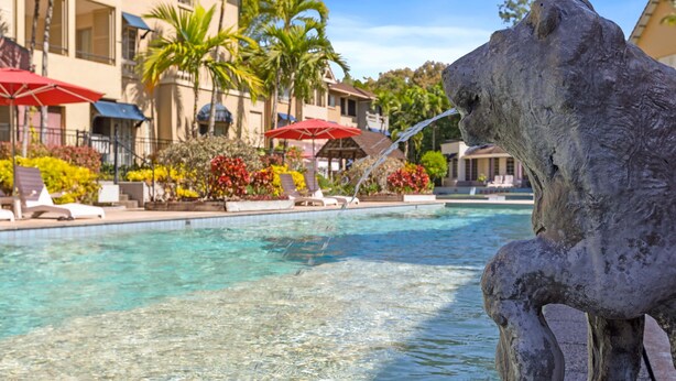 A swimming pool with clear water, surrounded by lounge chairs and umbrellas, with a building in the background. - Tropical Resort Escape (Cairns)