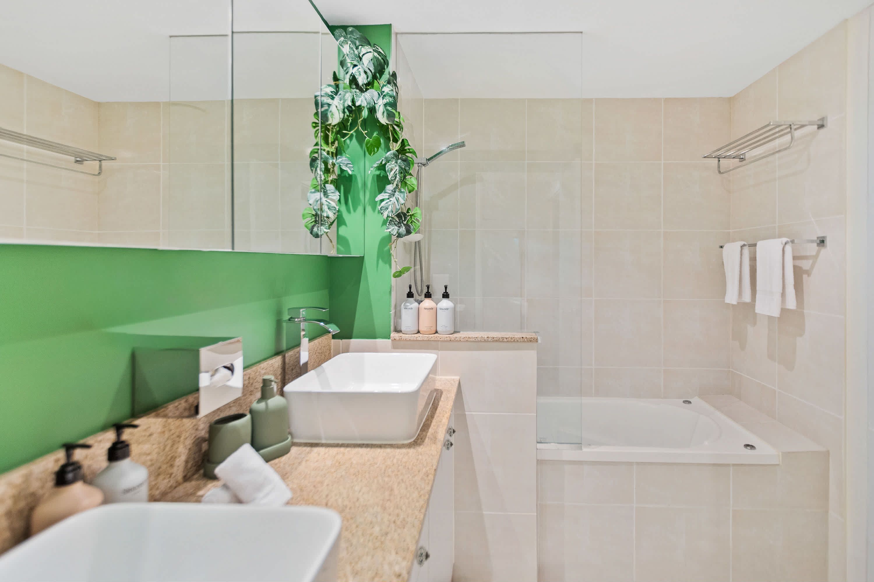 Uma casa de banho moderna com um espelho grande, duas pias, chuveiro e um jardim vertical verde.