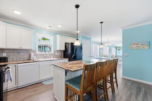 A kitchen with white cabinets, a granite countertop, and a dining area with wooden chairs. - Shackleford View Beach (Pet Friendly/Private Beach) (Harkers Island)