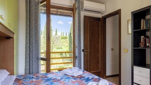 Ein Schlafzimmer mit einem Bett, einem Bücherregal und einer Tür, die auf einen Balkon mit Blick auf Bäume und Hügel führt.